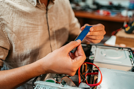 Close-up of a young man checking RAM and upgrading desktop computer in a workshop.