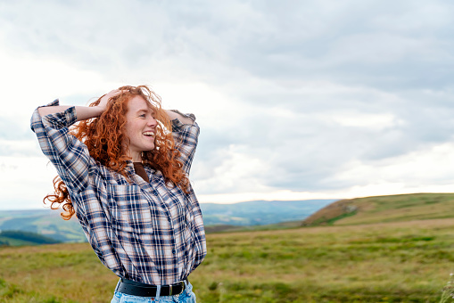 cheerful woman traveler in a white jacket and backpack traveling mountains and having a fun time in Peak District. Local tourism lifestyle concept.