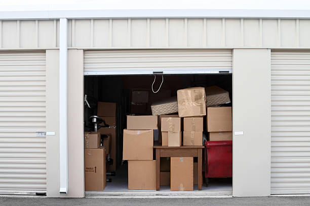 Self storage warehouse building with an open unit. Warehouse building with self storage units. Self storage facility. Roll up doors on self storage facility. One door open with boxes and furniture in doorway.  storage compartment stock pictures, royalty-free photos & images