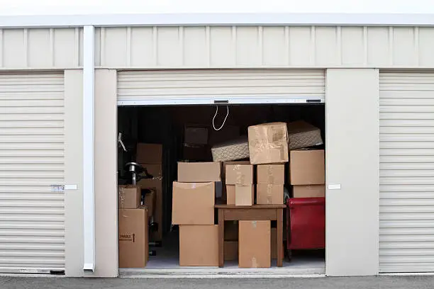 Warehouse building with self storage units. Self storage facility. Roll up doors on self storage facility. One door open with boxes and furniture in doorway. 