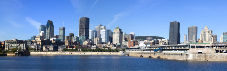A DSLR panoramic picture of Montreal Cityscape. The St-Lawrence river is in the foreground of the picture. Downtown Montreal and Old Montreal are in the background. It is a beautiful fall day and the sky is blue and clouded. The natural light of the day is making the city look luminous. 