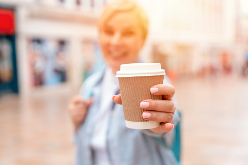 a happy woman in blue shirt with backpack with coffee under a walking around a modern city
