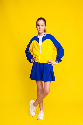 tennis player girl in sport wear stand in full height over yellow background