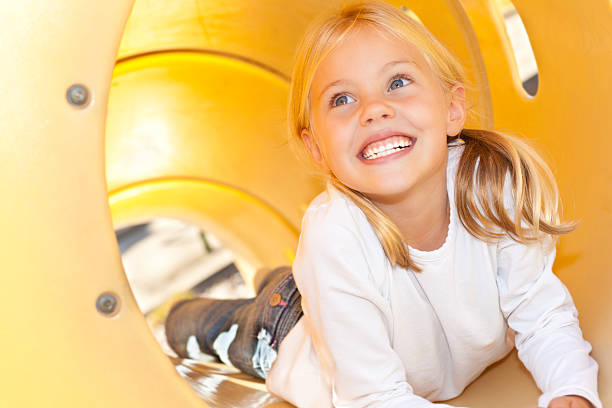 Little Giril With Pig Tails Playing In A yellow Slide At A Playground.