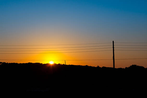 Crispy image of a power line and telephone line against a clear and colourful sunset.
