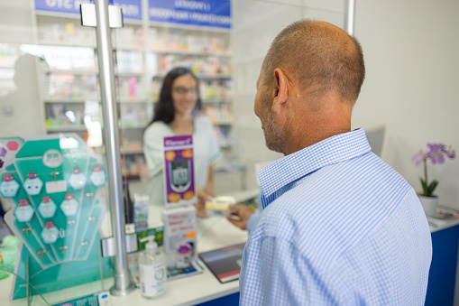 Multiethnic group of clients paying for medication with credit card, smartwatch and nfc with telephone. People waiting in line to buy pharmaceutical products in pharmacy retail store. Tripod shot.