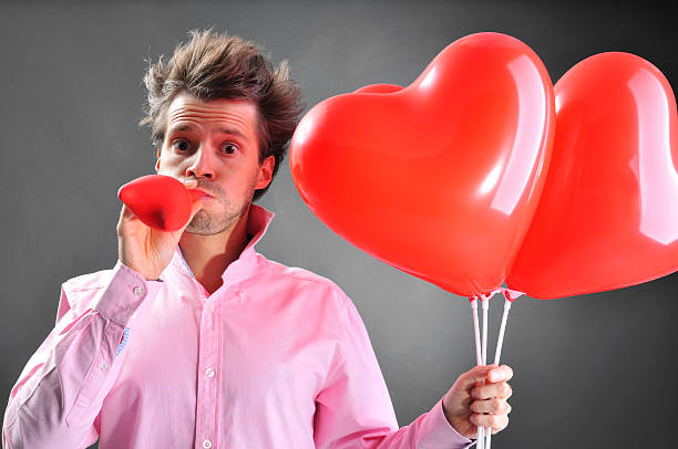 istock Man holding red heart-shaped balloons, he is inflating another one 157677686