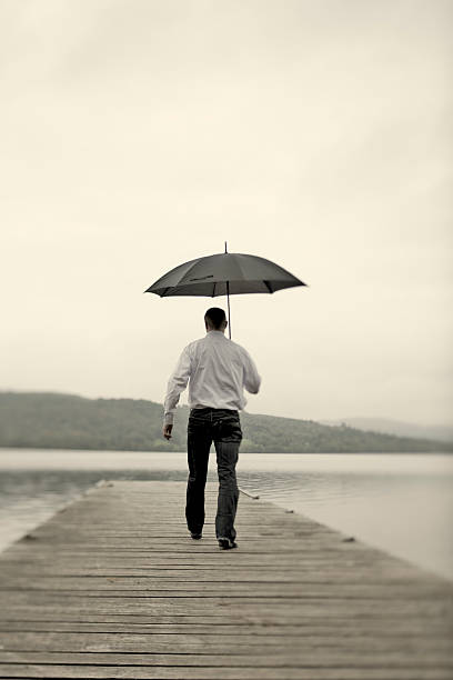 istock Solitude; Man with umbrella on wooden Jetty 157677700