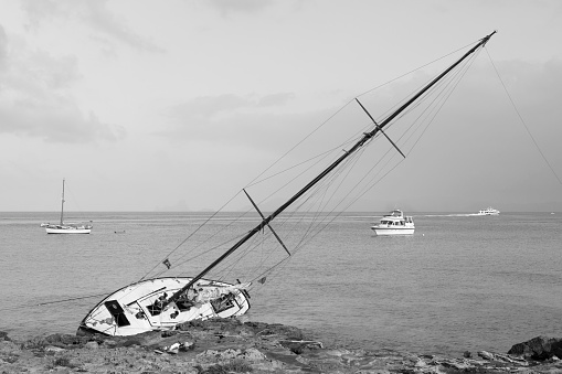Wooden sailboat aground on the rocks in the Mediterranean sea.