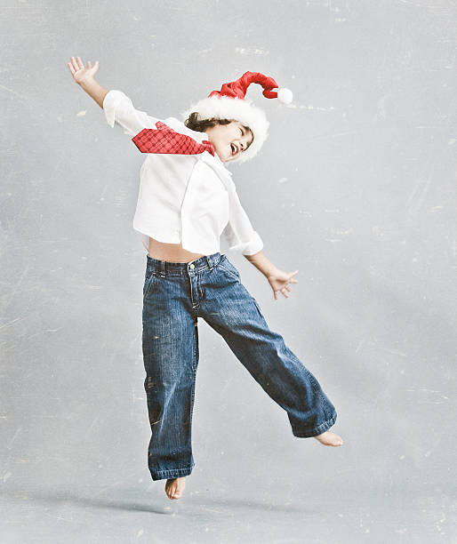 a barefoot hispanic kid dress with jeans, white shirt and santa hat - dancing and jumping on a gray background