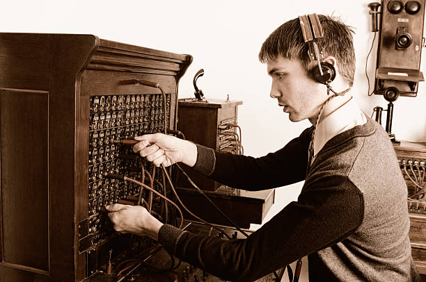 Telephone operator using antique switchboard Young man operating vintage telephone equipment switchboard operator stock pictures, royalty-free photos & images