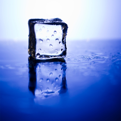 Cold, melting ice cube reflecting in blue.