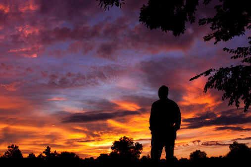 This silhouetted male watches and enjoys an early morning sunrise and a sky filled with spectacularly saturated colors.