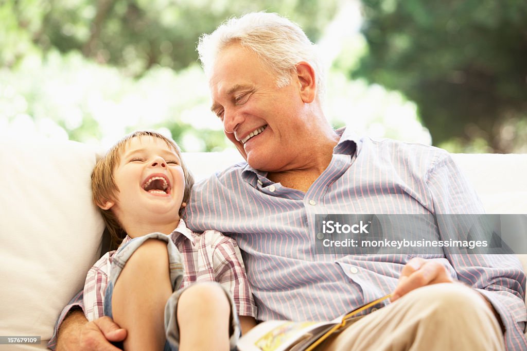 Grandfather With Grandson Reading Together On Sofa Grandfather With Grandson Reading Together On Sofa Laughing Grandfather Stock Photo