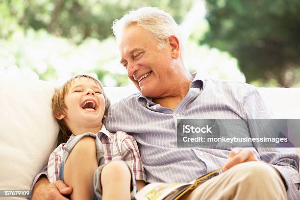 Grandfather With Grandson Reading Together On Sofa Stock Photo - Download Image Now - Grandfather, Senior Adult, Grandson