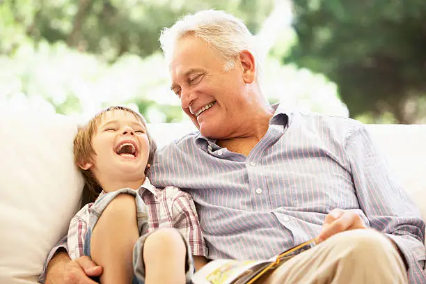 Grandfather With Grandson Reading Together On Sofa Laughing