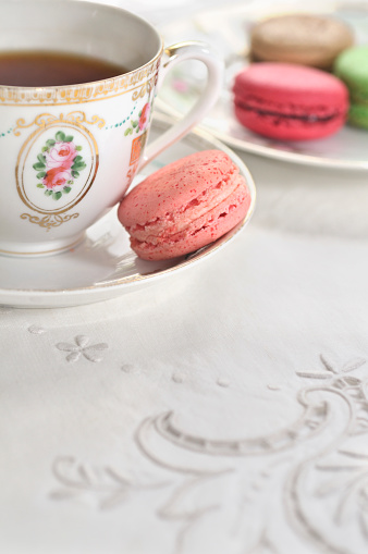 Elegant cup of tea and macarons on embroidered linen tablecloth