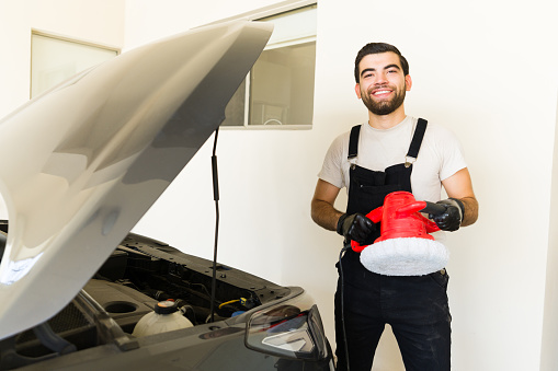 Young hispanic male employees with polishing tool shining customer's car at auto detail service
