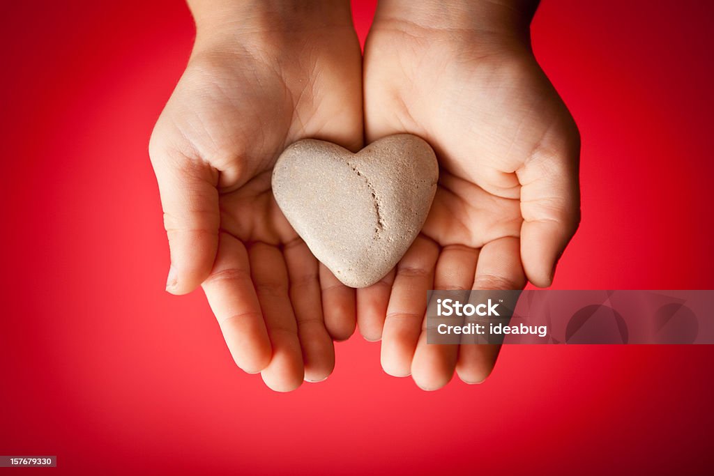 Child's Hands Holding a Heart-Shaped Rock on Red Background Color photo of a young child's hands holding a heart-shaped rock over a red background. Heart Shape Stock Photo