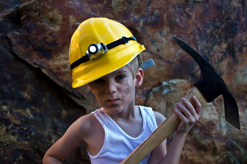 A kid wearing an engineer dress and attire portraying as a professional contractor. wearing a helmet and holding a yellow ruler in his hand acting like a builder and real estate engineer.