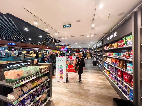 Sabiha Gokcen Airport, Istanbul, Turkey, 01/29/2023; Passengers waiting for their flight and walking through a large duty free shop displaying many packaged food products at SAW International Airport. Travel and Aviation delay concept. Tourism background, copy space.
