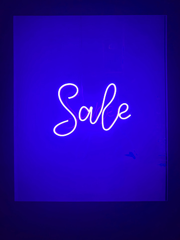 Sales concept: Bright illuminated neon sales text lighting on colored background with dark frame and large copy space. Advertising and marketing 3D illustration poster design