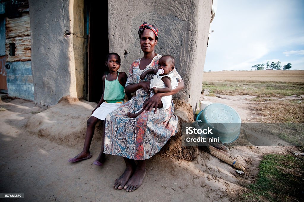 Poor African family sitting in front of a shanty hut Poor African family, mother with baby and little girl sitting outside their hut. Africa Stock Photo