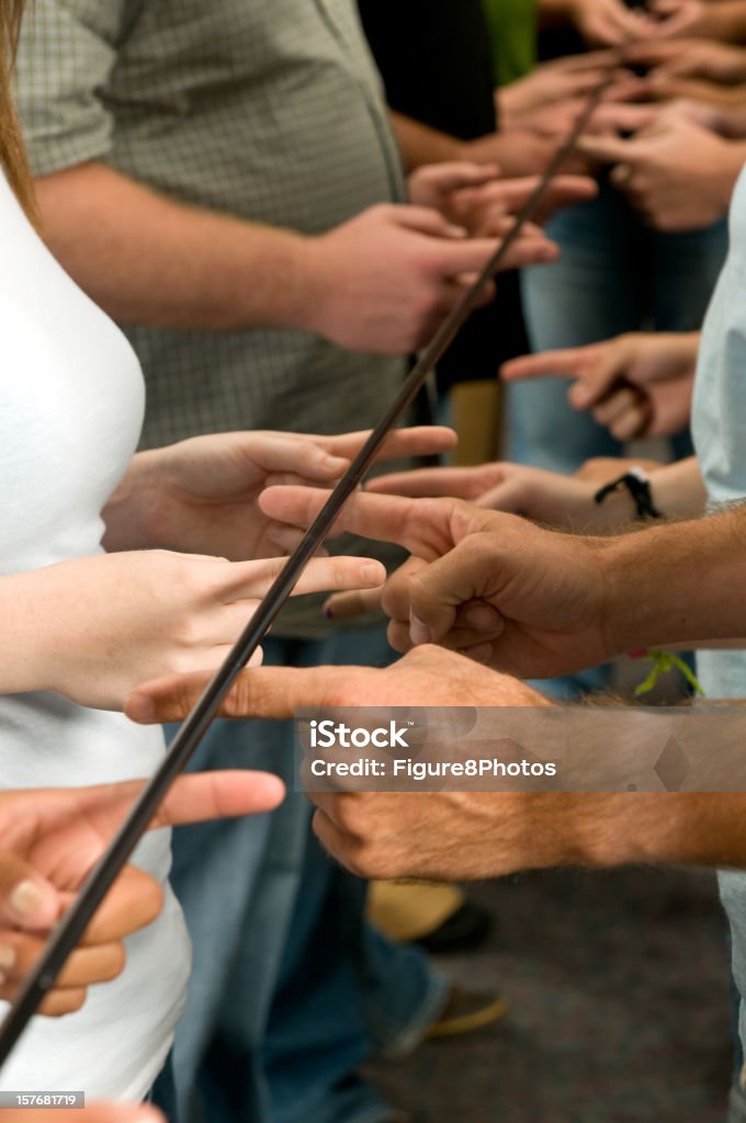 Fingers under pole Group of people working on a problem solving activity trying to lower the pole to the ground while staying in contact with the pole. (Focus is on Fingers) Adult Stock Photo