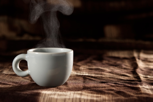 A cup of coffee with steam on brown tablecloth with copy space.