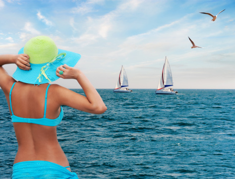 Young Woman Wearing In Blue Bikini And Hat Looking At Sailing Regatta