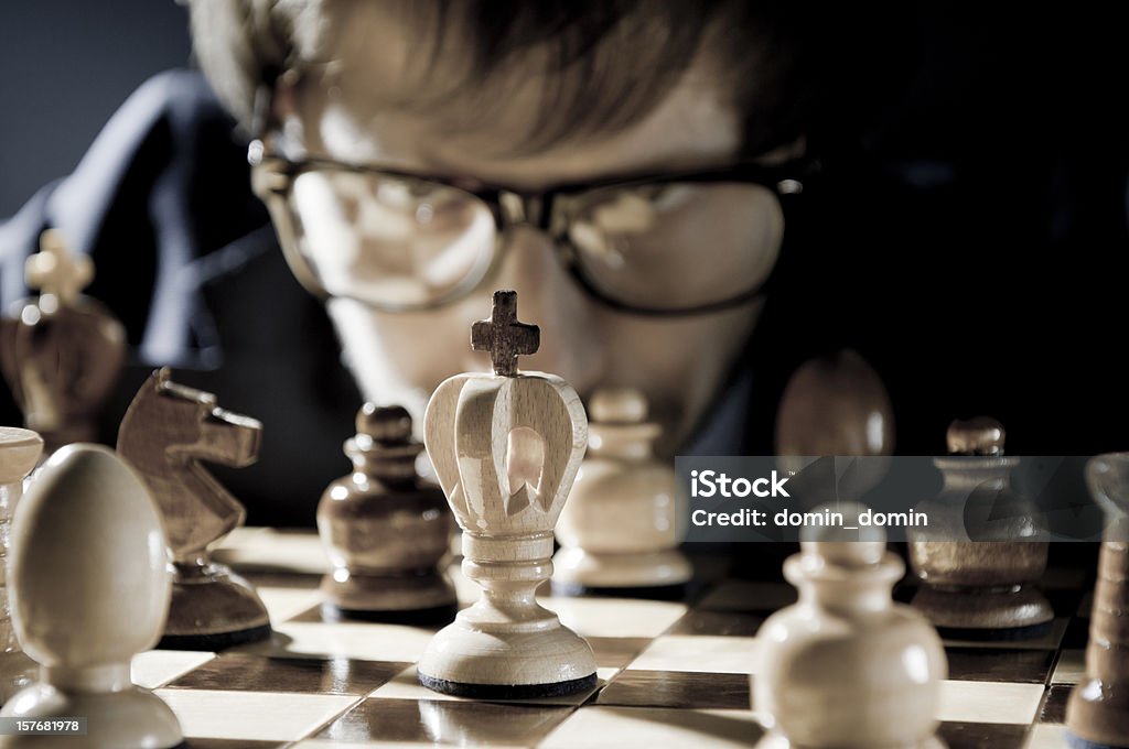 Chess competition, player in glasses thinking about next move Young chess player in horn rimmed glasses is thinking about his next move. Chessboard and figures. Little grain visible. Chess Stock Photo