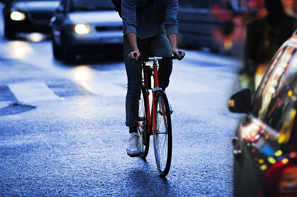 giovane adulto in bicicletta in città piovosa sera traffico - dividing line single line striped in a row foto e immagini stock