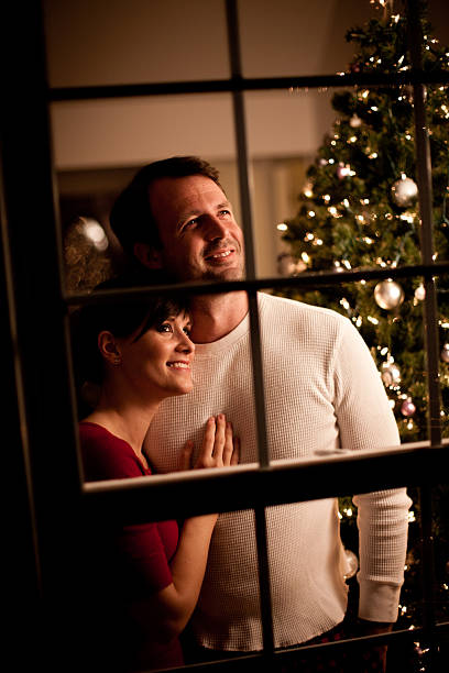 istock Happy Couple Looking Out Window with Christmas Tree Behind 157682181