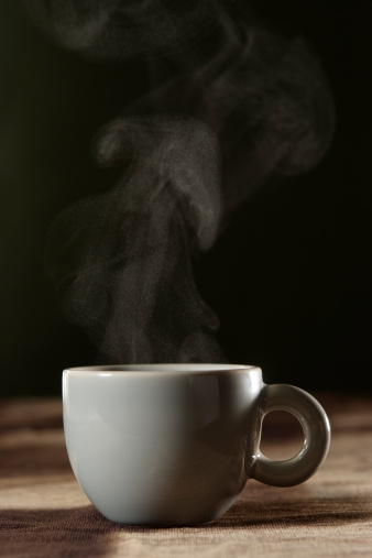 A cup of coffee with steam on brown tablecloth with copy space.