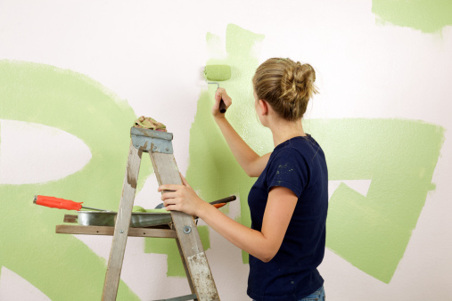 Mid-teen girl  holds a paint roller as she paints her room green facing away from the camera