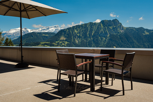 Empty terrace with a table, chairs and umbrella. Stunning view on the Diablerets massif in the Swiss Alps. Leysin, Vaud, Switzerland