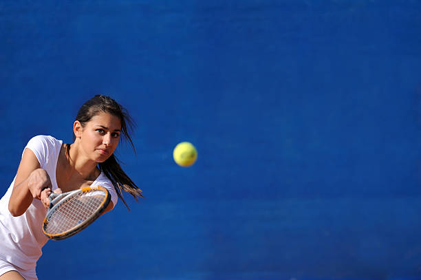 A sporty young woman dressed in a white shirt and black leggings hits a tennis ball on an outdoor court