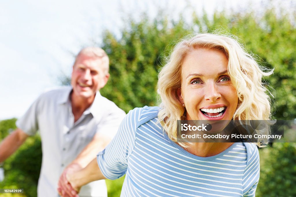 Cheerful woman holding hand of a senior man against sky  Senior Couple Stock Photo