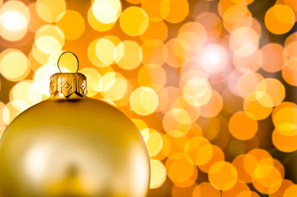 Single, golden Christmas bauble on warm, gold and orange lights background.