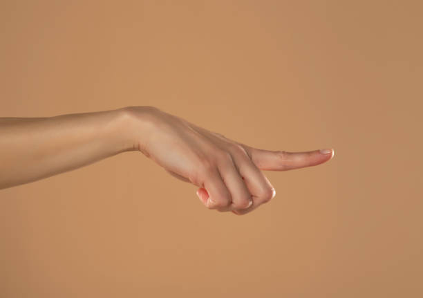 istock Young woman's palm touching imaginary product with index finger. Isolated on beige background 1576838316