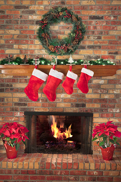 Red Christmas Stockings Fireplace Fire Wreath Poinsettias Mantel Decorations Hearth Four red Christmas stockings are hung above the fireplace, with an inviting fire.  The festive decorations include a large wreath, lighted garland, and two red poinsettia plants. red poinsettia vibrant color flower stock pictures, royalty-free photos & images