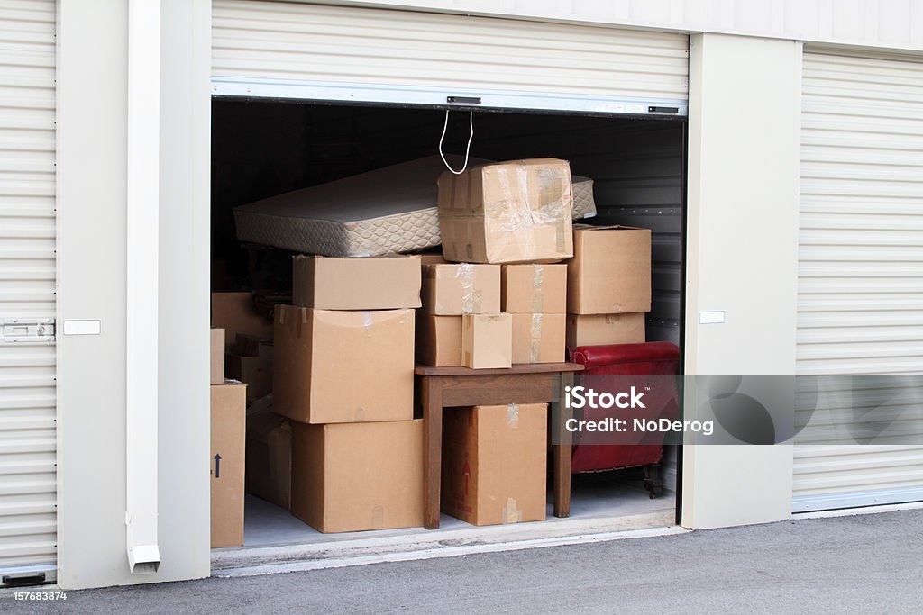 Self storage warehouse building with an open unit. Warehouse building with self storage units. Self storage facility. Roll up door open with boxes and furniture in doorway.  Storage Compartment Stock Photo