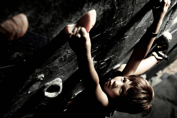 A young athlete guy climbs up a training wall for climbing with many hooks. View from below