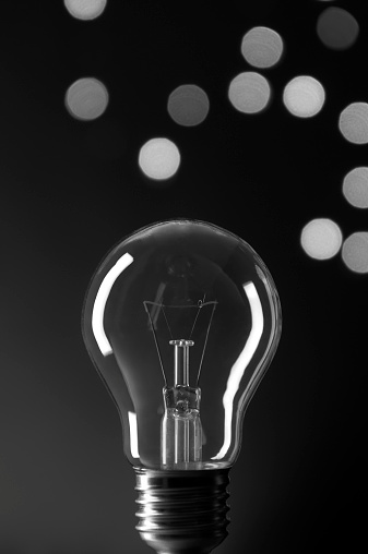 Light bulb on black background with defocused lights in black and white.