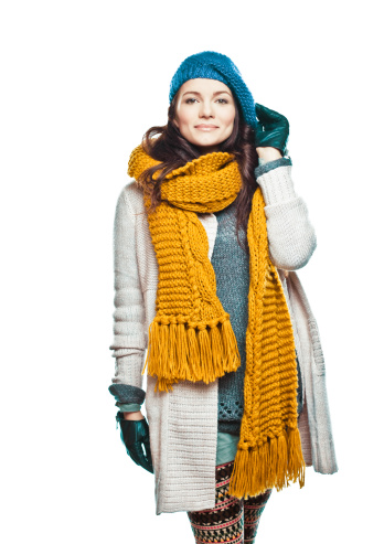 A beautiful young brunette wearing knit hat, scarf, pullower and gloves posing against the white background. Looking at camera and smiling, Studio shot.