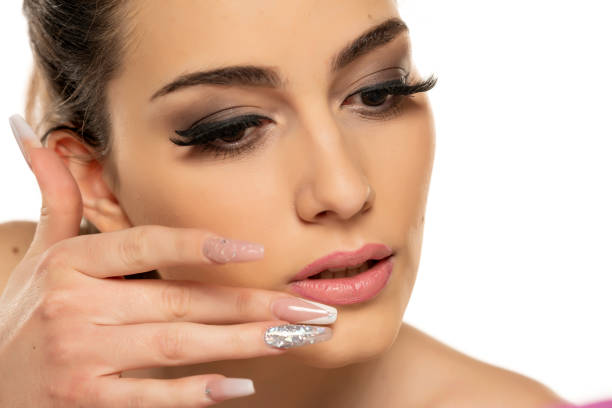 a young woman corrects lipgloss on her lips with her finger on a white background.