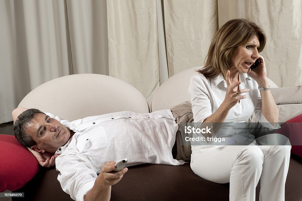 Homem assistindo televisão enquanto mulher fala pelo telefone - Foto de stock de Assistir TV royalty-free