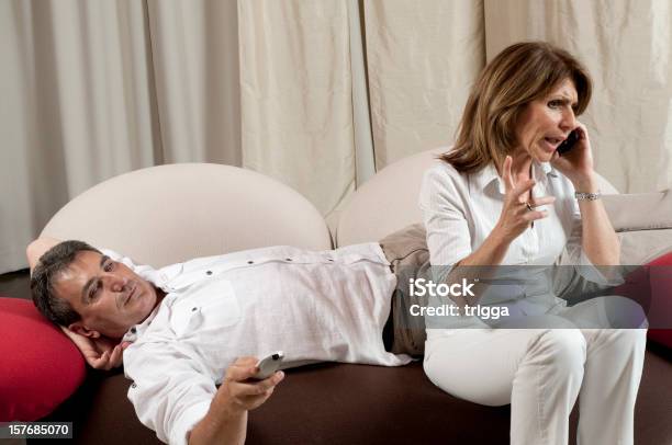 Foto de Homem Assistindo Televisão Enquanto Mulher Fala Pelo Telefone e mais fotos de stock de Assistir TV