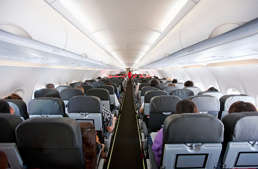 Passengers inside the cabin of a commercial airliner during flight. Shallow depth of field with focus on the seats in the foreground.