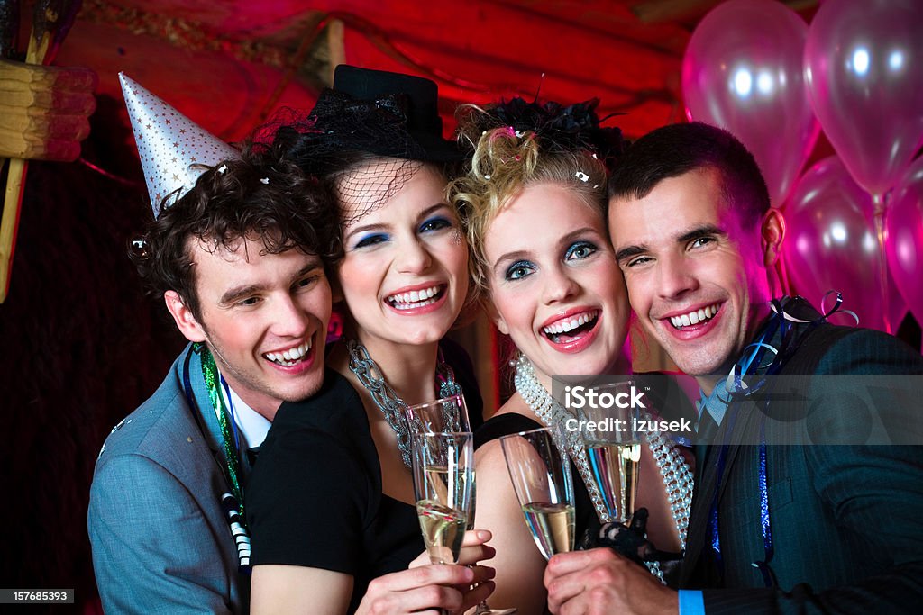 Happy New Year! A well dressed young people celebrating New Year's Day. They standing against balloons and toasting with champagne glasses. Looking at camera and laughing.  Adult Stock Photo